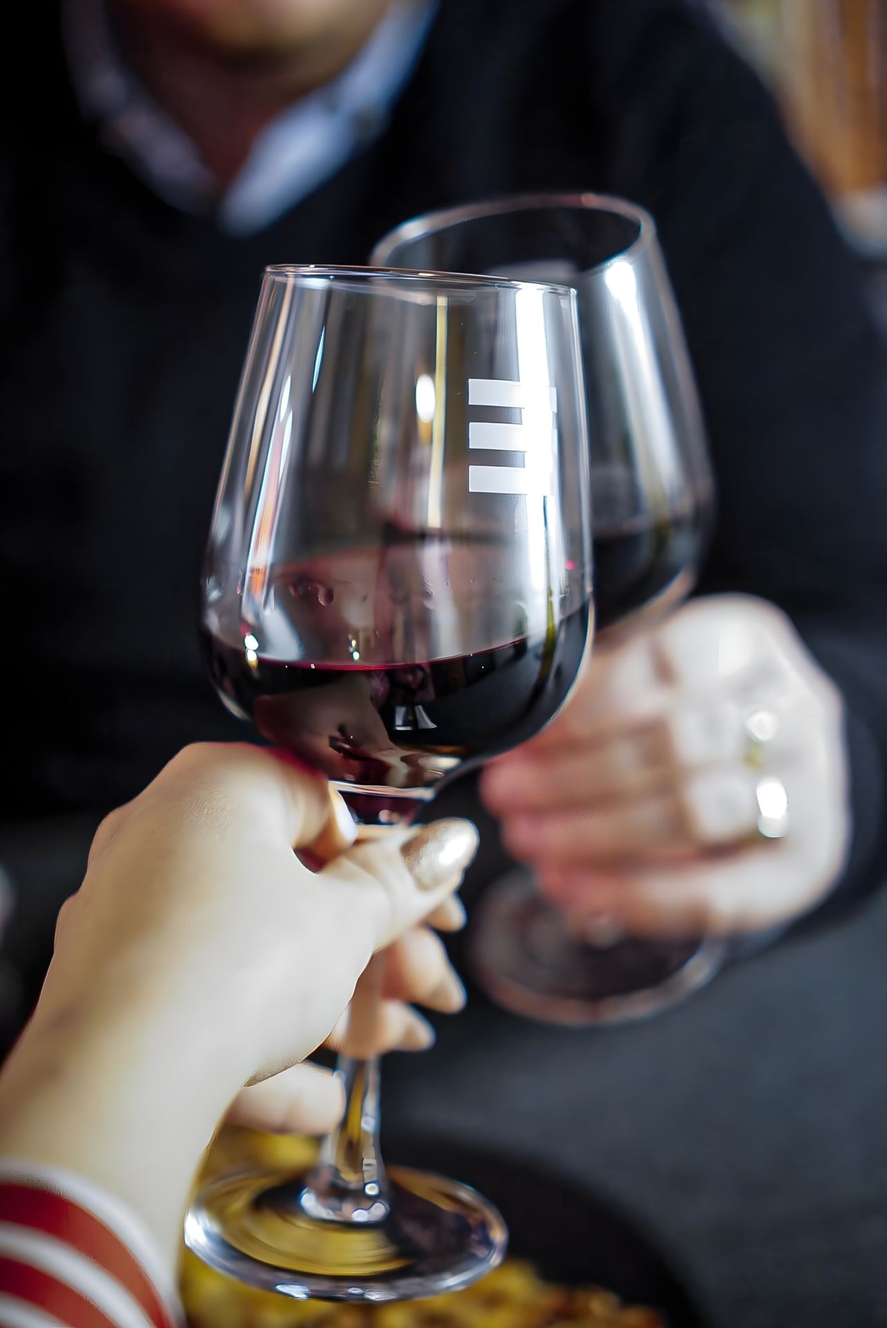Two people toasting with glasses of red wine at a table in a cozy setting.